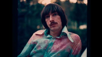 Movie still from “The Velvet Underground” (2021), directed by Todd Haynes – A man with long black hair wearing a pink and blue shirt; Close Up shot, Low angle