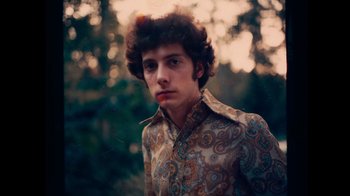 Movie still from “The Velvet Underground” (2021), directed by Todd Haynes – A young man in a floral shirt is standing in a wooded area; Close Up shot, Low angle