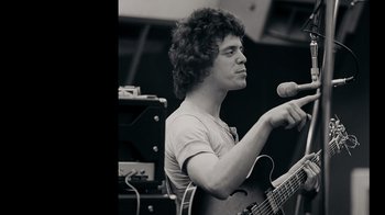 Movie still from “The Velvet Underground” (2021), directed by Todd Haynes – A man holding a microphone while holding a guitar; Close Up shot, Low angle