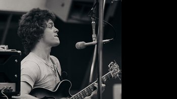 Movie still from “The Velvet Underground” (2021), directed by Todd Haynes – A man holding a guitar in front of a microphone; Close Up shot, Low angle