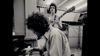 Movie still from “The Velvet Underground” (2021), directed by Todd Haynes – A man playing a guitar while another man plays a keyboard; Medium shot, Low angle
