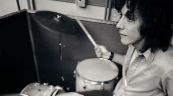 Movie still from “The Velvet Underground” (2021), directed by Todd Haynes – A man is playing drums in a black and white photo; Close Up shot, Low angle