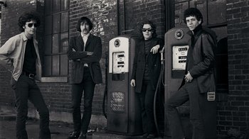 Movie still from “The Velvet Underground” (2021), directed by Todd Haynes – A group of men standing next to each other near gas pumps; Medium shot, Low angle