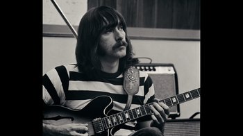 Movie still from “The Velvet Underground” (2021), directed by Todd Haynes – Black and white photograph of a man holding a guitar; Close Up shot, High angle