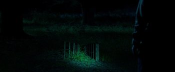 Movie still from “The Visitor” (2022), directed by Justin P. Lange – A dark picture of grass and a fence; Extreme Wide shot, High angle