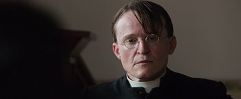 Movie still from “The Water Diviner” (2014), directed by Russell Crowe – A man wearing glasses and a priest's outfit; Close Up shot, Low angle