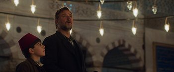 Movie still from “The Water Diviner” (2014), directed by Russell Crowe – A man in a suit and tie standing in front of lights; Medium shot, Low angle