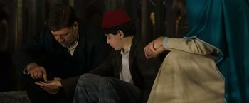 Movie still from “The Water Diviner” (2014), directed by Russell Crowe – A young boy wearing a red fez sitting next to an older man; Medium shot, Over the shoulder angle