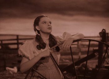 Movie still from “The Wizard of Oz” (1939), directed by Victor Fleming – A young girl in a dress is standing by a railing; Medium shot, Low angle