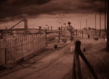 Movie still from “The Wizard of Oz” (1939), directed by Victor Fleming – A man riding a bike down a dirt road; Wide shot, Low angle