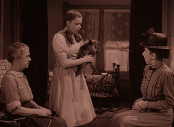 Movie still from “The Wizard of Oz” (1939), directed by Victor Fleming – A woman holding a small dog while sitting next to two other women; Medium shot, High angle