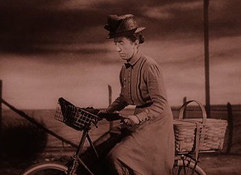 Movie still from “The Wizard of Oz” (1939), directed by Victor Fleming – An old photo of a woman riding a bike; Medium shot, Low angle