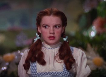 Movie still from “The Wizard of Oz” (1939), directed by Victor Fleming – A woman with long red pigtails wearing a blue and white dress; Close Up shot, Low angle