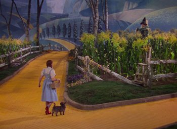 Movie still from “The Wizard of Oz” (1939), directed by Victor Fleming – A woman walking down a yellow brick road with a black cat; Wide shot, Low angle