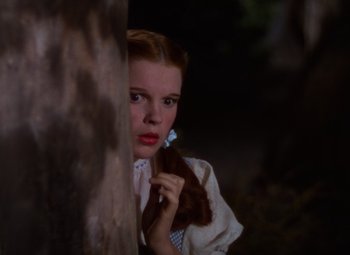 Movie still from “The Wizard of Oz” (1939), directed by Victor Fleming – A young girl in a white dress holding a blue object; Close Up shot, Low angle