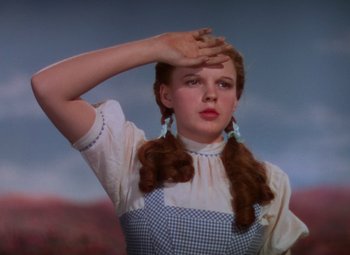 Movie still from “The Wizard of Oz” (1939), directed by Victor Fleming – A young woman in an old fashioned dress with her hand up to her forehead; Close Up shot, Low angle