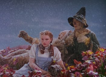 Movie still from “The Wizard of Oz” (1939), directed by Victor Fleming – A woman sitting next to a man dressed as the wizard of oz; Wide shot, Low angle