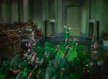 Movie still from “The Wizard of Oz” (1939), directed by Victor Fleming – A group of people dressed in green are sitting in a room; Extreme Wide shot, High angle