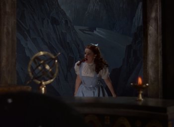 Movie still from “The Wizard of Oz” (1939), directed by Victor Fleming – A woman standing in front of a mirror with mountains in the background; Medium shot, Low angle