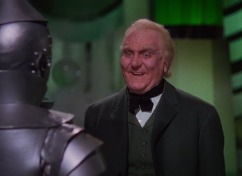 Movie still from “The Wizard of Oz” (1939), directed by Victor Fleming – A man in a green suit and a black tie standing in front of a man in a metal suit; Medium shot, Low angle