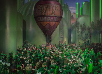Movie still from “The Wizard of Oz” (1939), directed by Victor Fleming – A crowd of people in green costumes and a hot air balloon in the sky; Extreme Wide shot, High angle