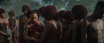 Movie still from “The Woman King” (2022), directed by Gina Prince-Bythewood – A group of people with long hair are gathered together; Medium shot, Over the shoulder angle