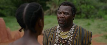 Movie still from “The Woman King” (2022), directed by Gina Prince-Bythewood – An older man wearing a necklace talking to a young woman; Close Up shot, Over the shoulder angle