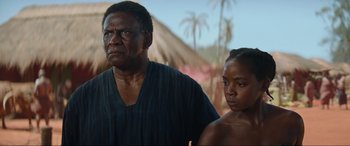 Movie still from “The Woman King” (2022), directed by Gina Prince-Bythewood – An older man and a young woman standing next to each other; Close Up shot, Over the shoulder angle