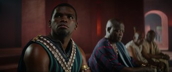 Movie still from “The Woman King” (2022), directed by Gina Prince-Bythewood – Two men are sitting in a room and one of them is wearing a necklace; Close Up shot, Low angle