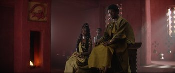 Movie still from “The Woman King” (2022), directed by Gina Prince-Bythewood – A couple of people sitting on top of a chair; Medium shot, Low angle