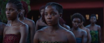 Movie still from “The Woman King” (2022), directed by Gina Prince-Bythewood – A young woman standing in front of a group of people; Close Up shot, Over the shoulder angle