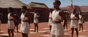 Movie still from “The Woman King” (2022), directed by Gina Prince-Bythewood – A group of young women standing on a dirt field; Medium shot, Over the shoulder angle