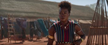 Movie still from “The Woman King” (2022), directed by Gina Prince-Bythewood – A woman in a colorful outfit standing in front of a wall; Close Up shot, Over the shoulder angle