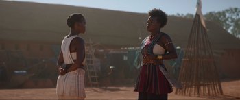 Movie still from “The Woman King” (2022), directed by Gina Prince-Bythewood – Two women standing next to each other on a dirt field; Medium shot, Over the shoulder angle