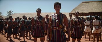 Movie still from “The Woman King” (2022), directed by Gina Prince-Bythewood – A group of men standing next to each other on top of a dirt field; Medium shot, Over the shoulder angle