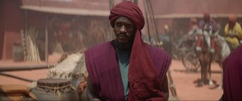 Movie still from “The Woman King” (2022), directed by Gina Prince-Bythewood – A man with a red turban on his head; Medium shot, Over the shoulder angle