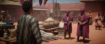 Movie still from “The Woman King” (2022), directed by Gina Prince-Bythewood – A man standing in front of a bunch of pots; Wide shot, Over the shoulder angle
