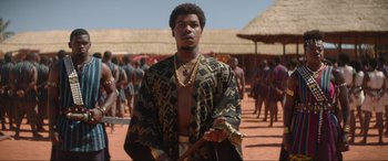 Movie still from “The Woman King” (2022), directed by Gina Prince-Bythewood – A man standing in front of a group of people; Medium shot, Over the shoulder angle