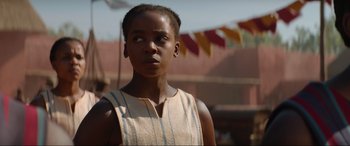 Movie still from “The Woman King” (2022), directed by Gina Prince-Bythewood – A young woman standing in front of a string of flags; Close Up shot, Low angle