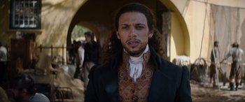 Movie still from “The Woman King” (2022), directed by Gina Prince-Bythewood – A man with long black hair wearing a suit and tie; Close Up shot, Low angle