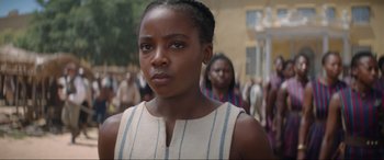 Movie still from “The Woman King” (2022), directed by Gina Prince-Bythewood – A young woman standing in front of a crowd of people; Close Up shot, Over the shoulder angle