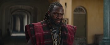 Movie still from “The Woman King” (2022), directed by Gina Prince-Bythewood – A man with a long beard wearing a red and black jacket; Close Up shot, Low angle