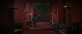 Movie still from “The Woman King” (2022), directed by Gina Prince-Bythewood – A woman in a green dress walking through a doorway; Extreme Wide shot, Over the shoulder angle