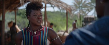 Movie still from “The Woman King” (2022), directed by Gina Prince-Bythewood – A woman in a multicolored shirt is standing outside; Close Up shot, Over the shoulder angle