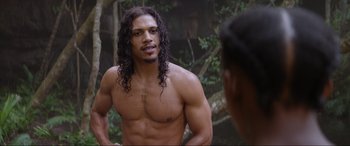 Movie still from “The Woman King” (2022), directed by Gina Prince-Bythewood – A man with long black hair is looking at another man; Medium shot, Over the shoulder angle
