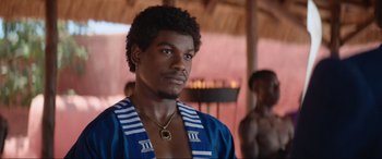 Movie still from “The Woman King” (2022), directed by Gina Prince-Bythewood – A man in a blue shirt is looking at the camera; Close Up shot, Over the shoulder angle