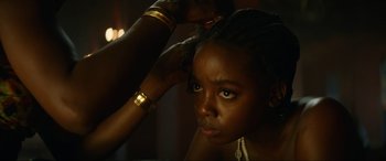 Movie still from “The Woman King” (2022), directed by Gina Prince-Bythewood – A young girl is getting her hair combed; Close Up shot, Over the shoulder angle