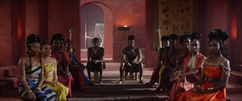 Movie still from “The Woman King” (2022), directed by Gina Prince-Bythewood – A group of men and women sitting on chairs in a room; Extreme Wide shot, Low angle