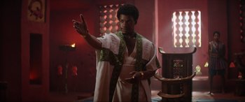 Movie still from “The Woman King” (2022), directed by Gina Prince-Bythewood – A man wearing a robe and holding his hand up; Medium shot, Low angle