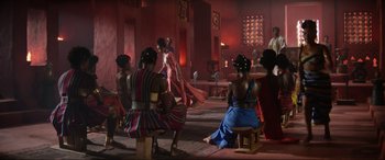 Movie still from “The Woman King” (2022), directed by Gina Prince-Bythewood – A group of people sitting around in a room; Extreme Wide shot, Over the shoulder angle